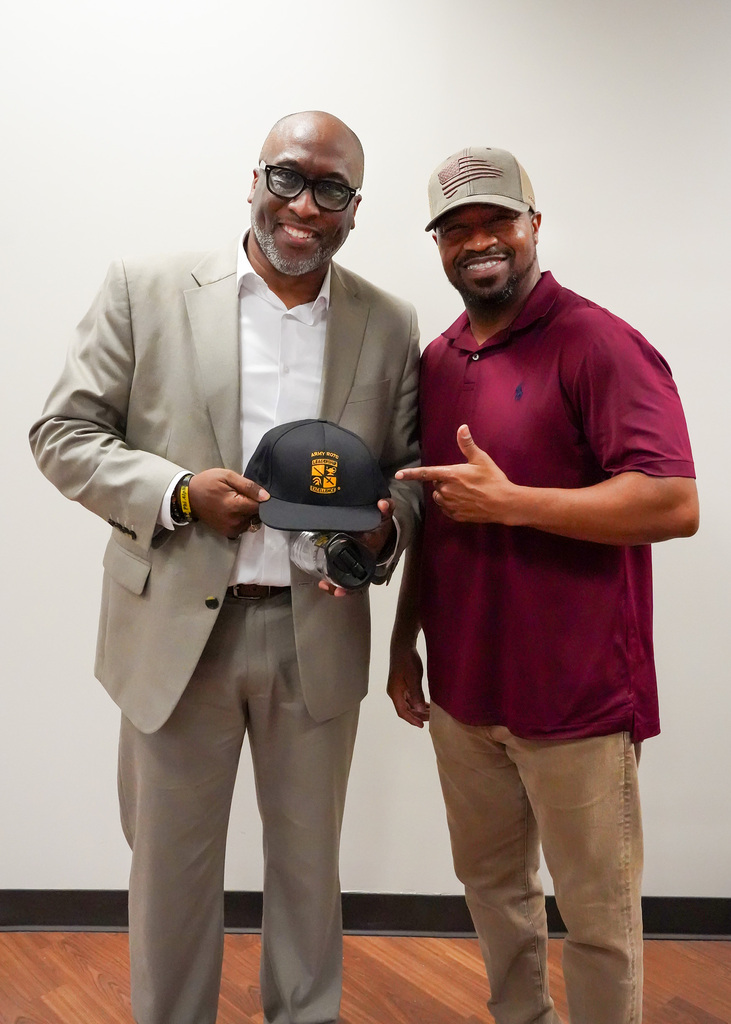 Mr. Bobby Jackson and a colleague smile for the camera while holding up an ROTC marine cap.