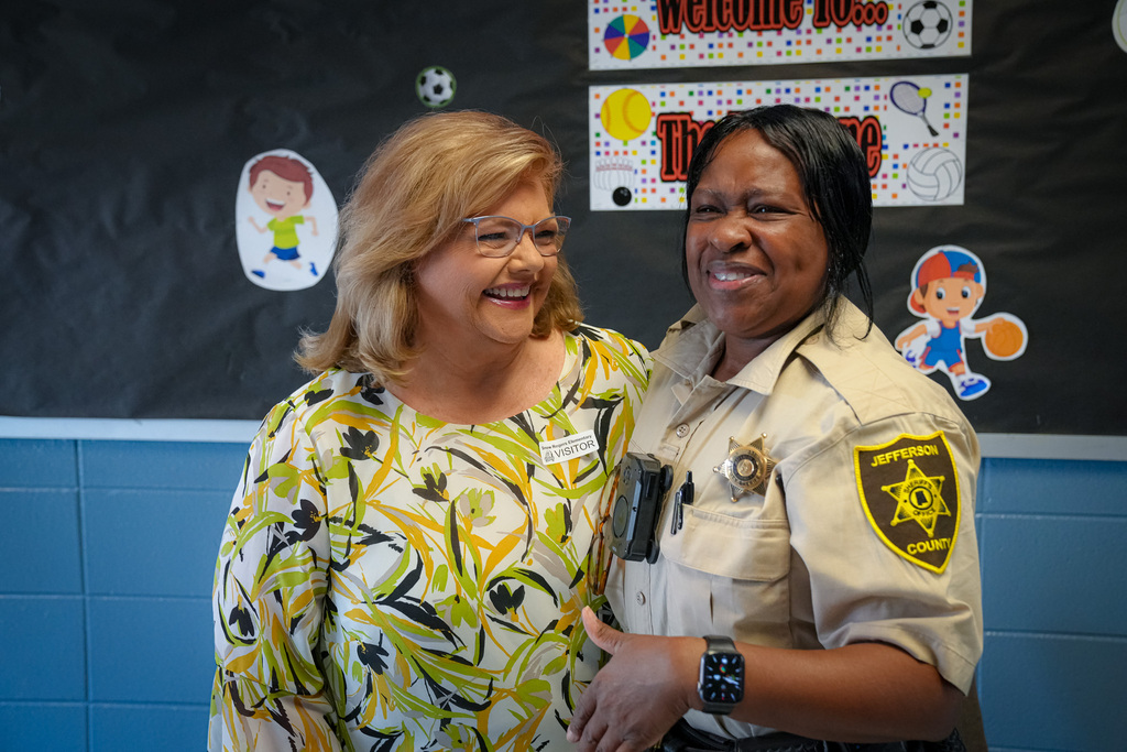 Two women hug while standing inside a school.