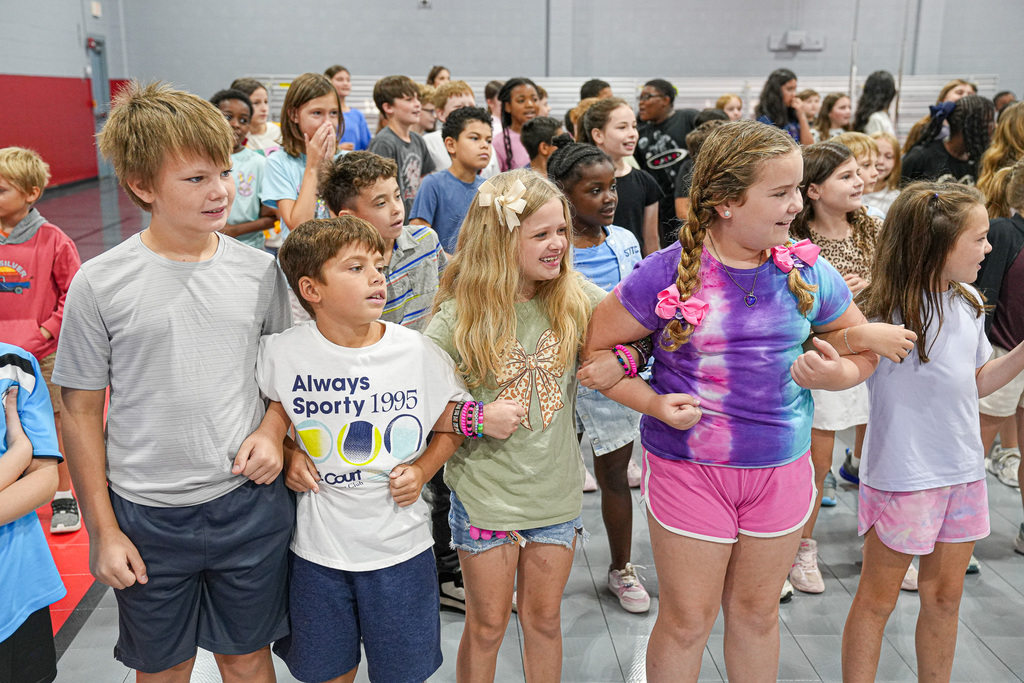 Students smile while standing in a school gym and linking arms.