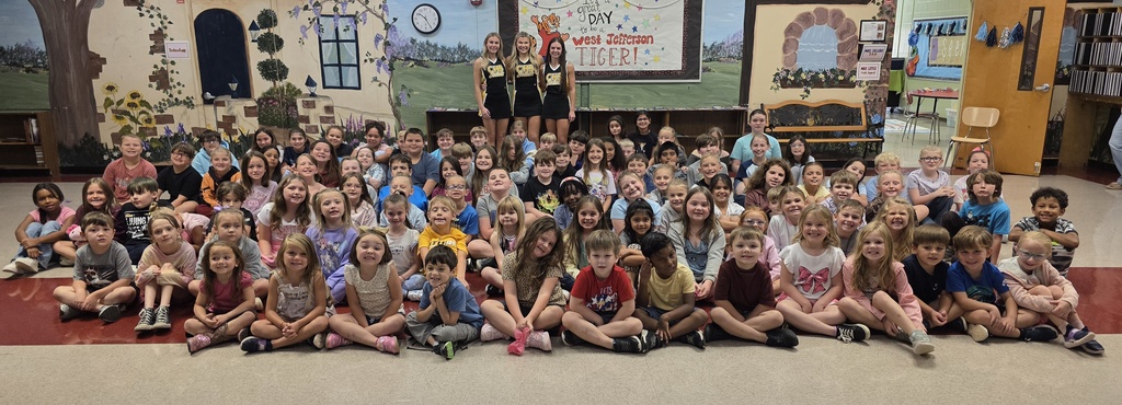large group of students sitting on the floor smiling with 3 cheerleaders standing behind them