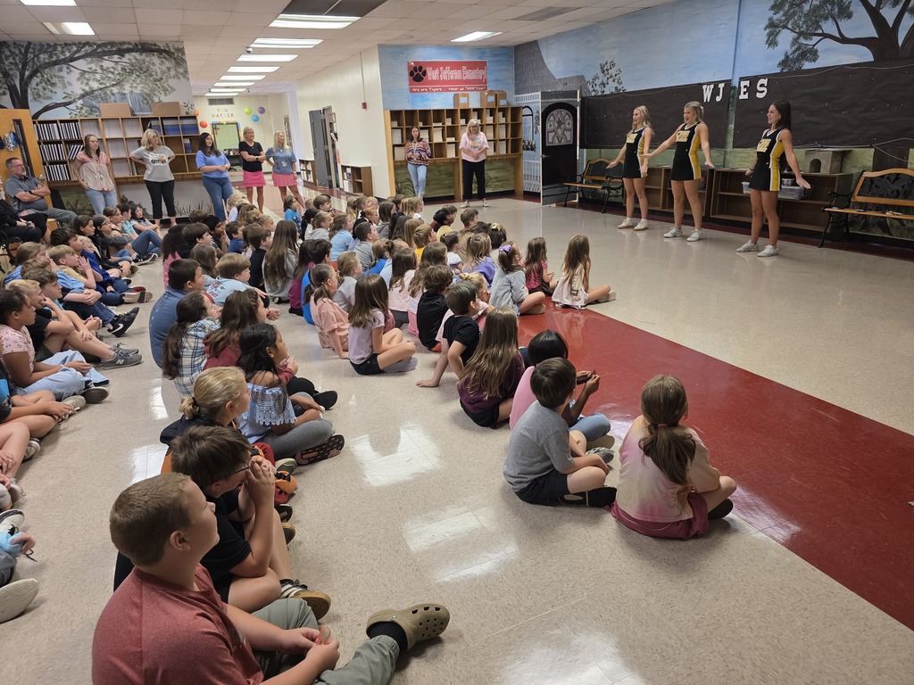 3 cheerleaders leading a cheer with students watching on