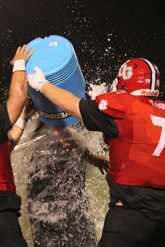 Football players pour water over a coach's head to celebrate his 100th career win.