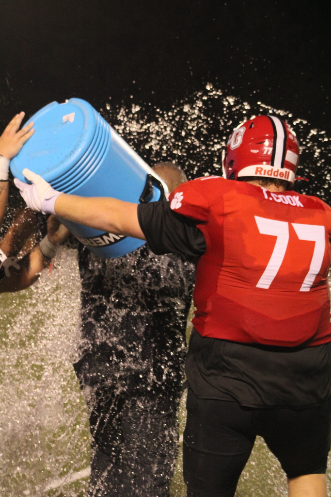 Football players pour water over a coach's head to celebrate his 100th career win.
