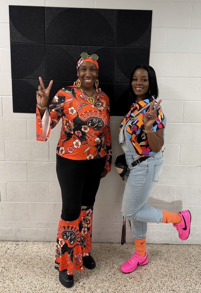 Two HMS staff members smile and pose in colorful retro outfits for Decades Day.