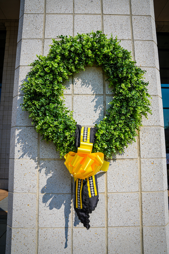 Close-up image of a wreath with a yellow ribbon hangs outside a school.