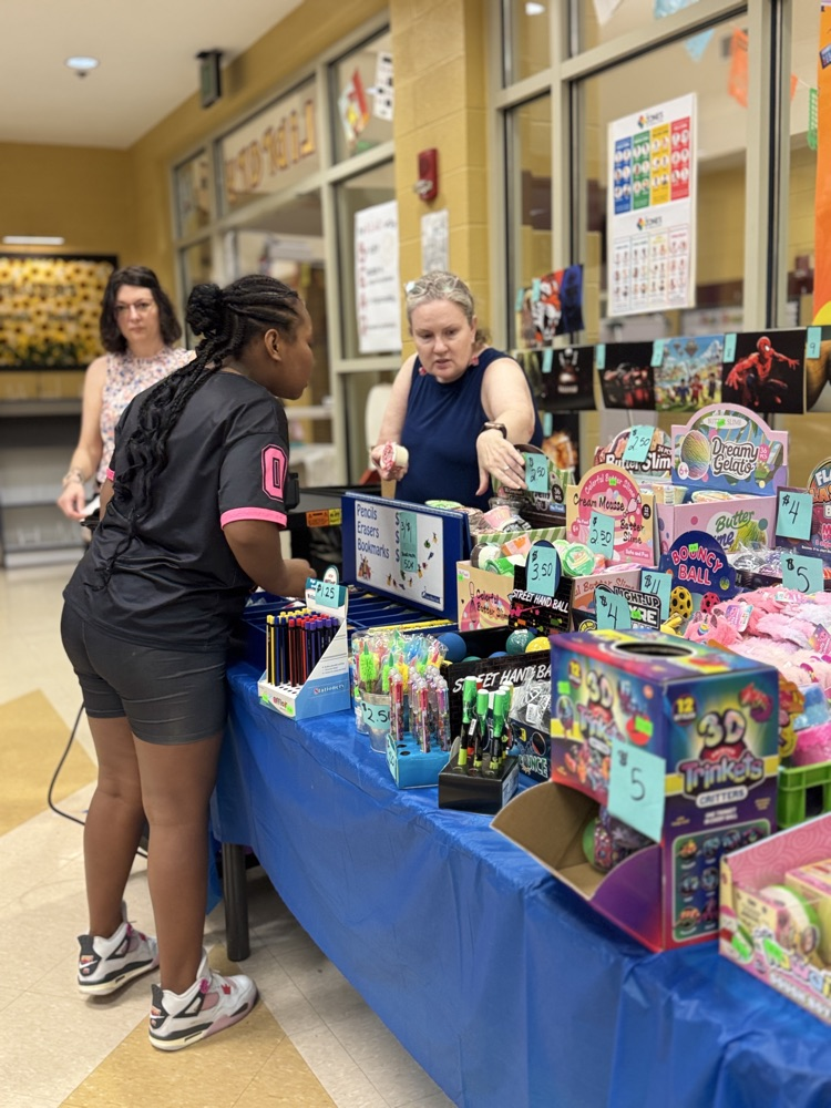 students and teachers looking at toys at the book fair in the library of a school