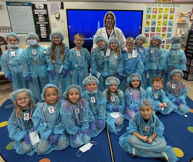 Mrs. Hughes and her first grade class smiling with doctor outfits and badges on