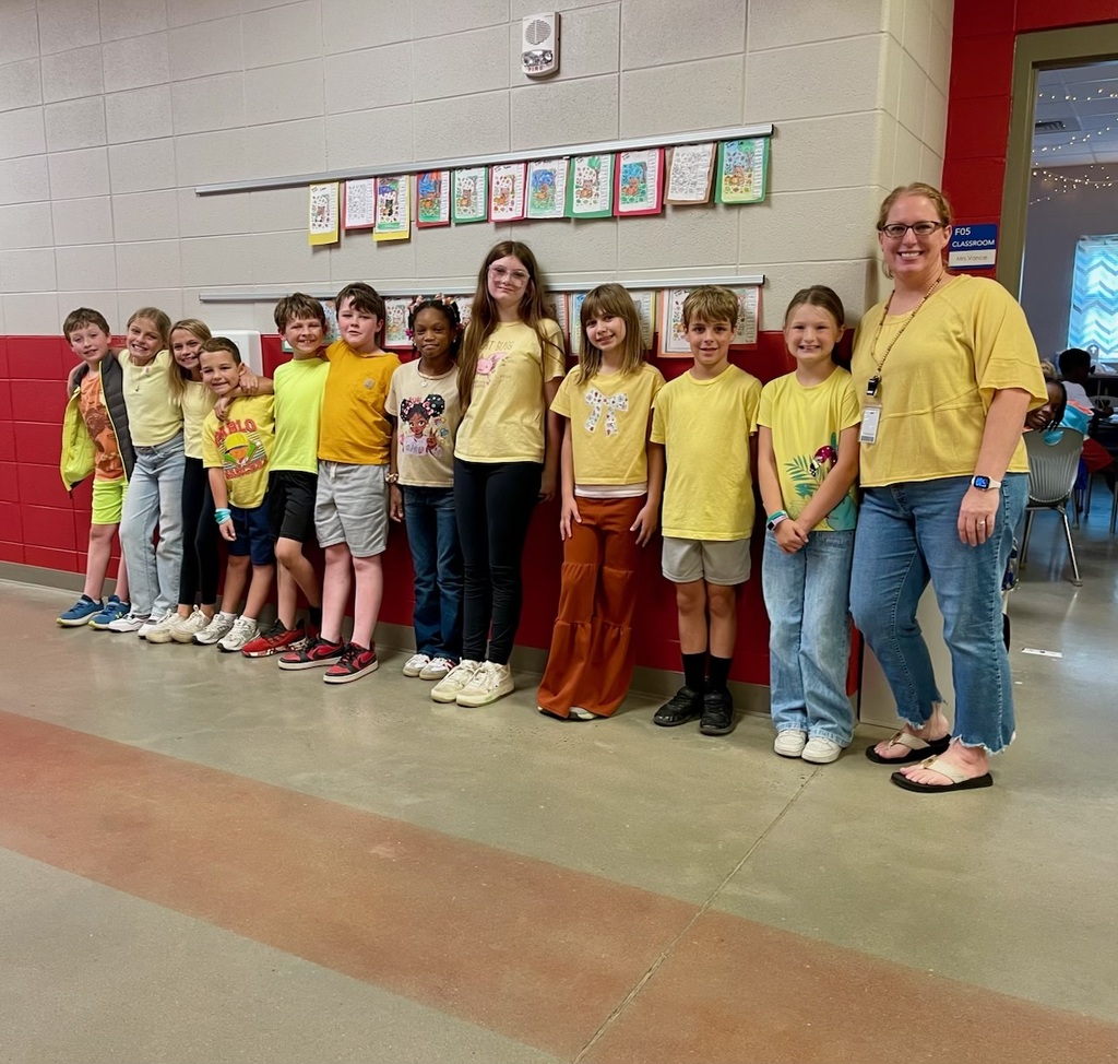 Teacher posing with class outside in the hallway showing their gold color clothing.