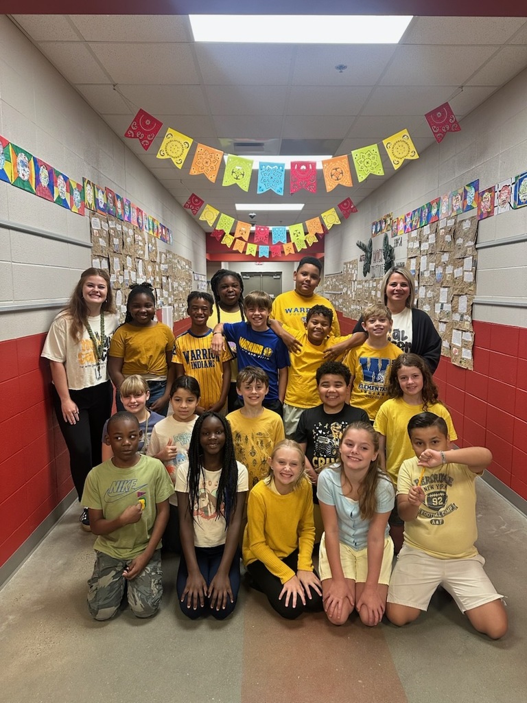 Teacher posing with class outside in the hallway showing their gold color clothing. 