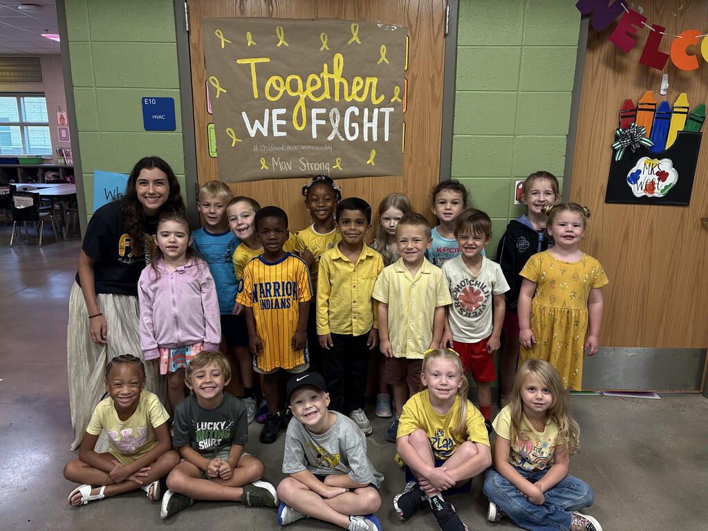 Teacher posing with class outside in the hallway showing their gold color clothing.
