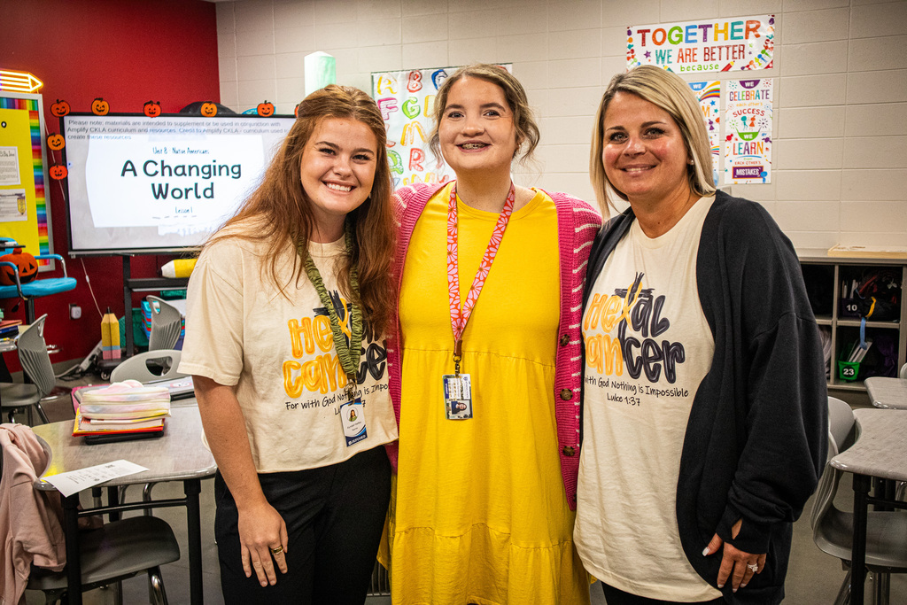 Educators wearing yellow smile for a photo inside a classroom.
