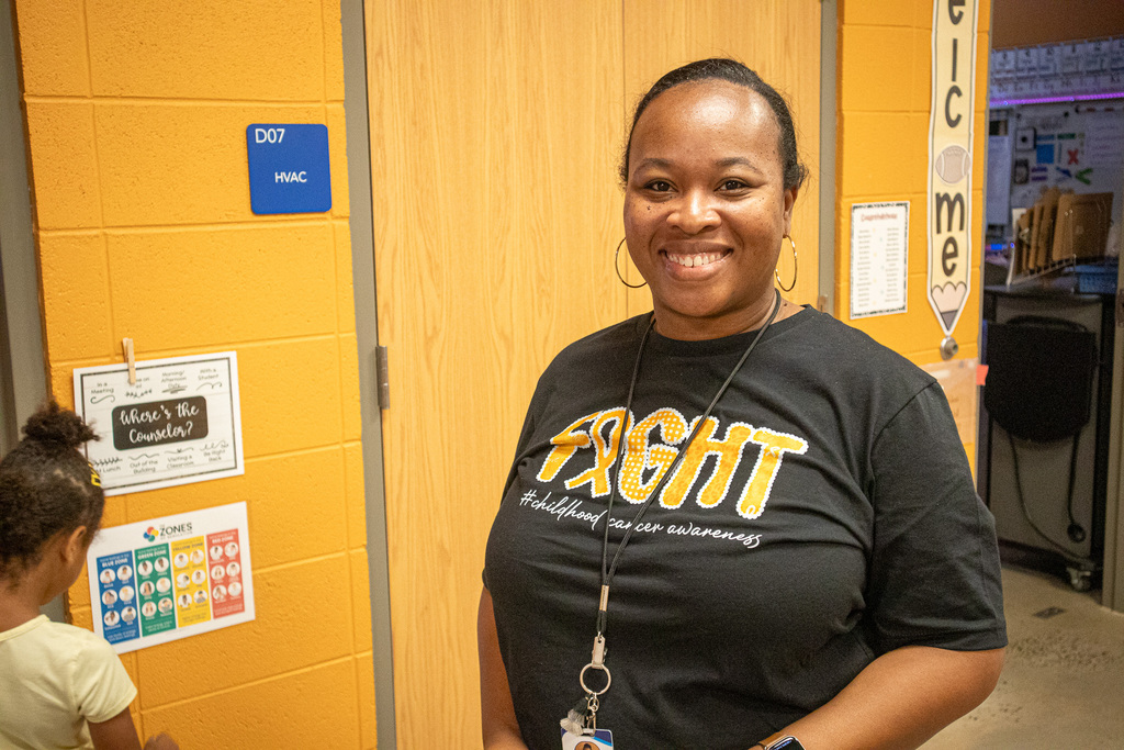 A woman wearing a Childhood Cancer awareness shirt smiles for a photo.