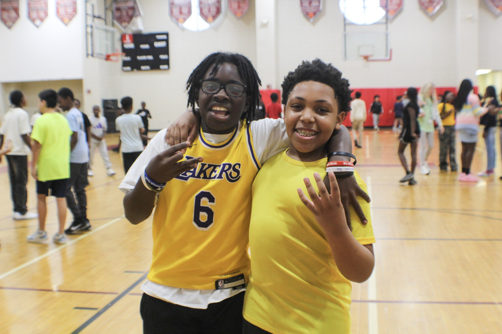 Children wearing yellow shirts smile for a photo in a school gym.