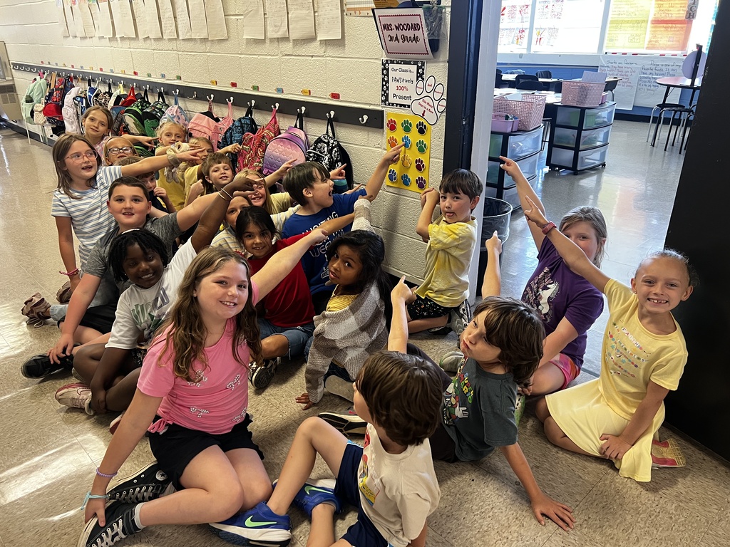 group of 2nd graders pointing to paw prints on the wall outside of their classroom.