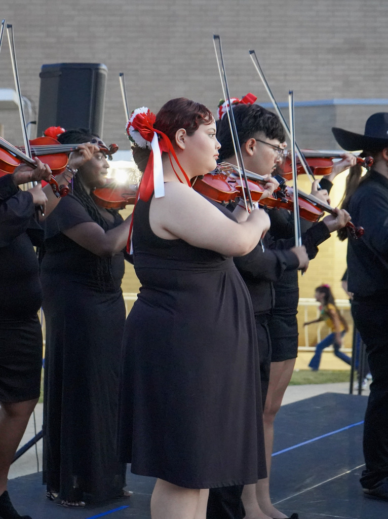 A mariachi band plays instruments on a stage outdoors.