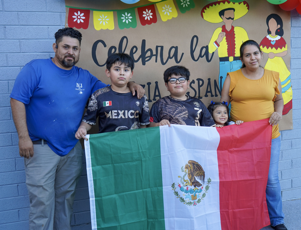A family stands together for a photo at a Hispanic Heritage Festival. They hold the Mexican flag.