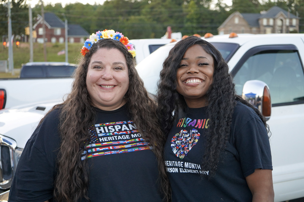 Two teachers smile for a photo while standing outside.