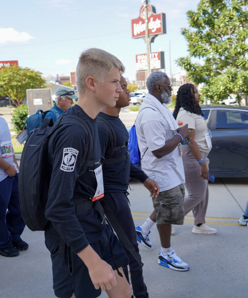 Students and community members walk down a street wearing weighted backpacks to honor veterans lost to suicide.