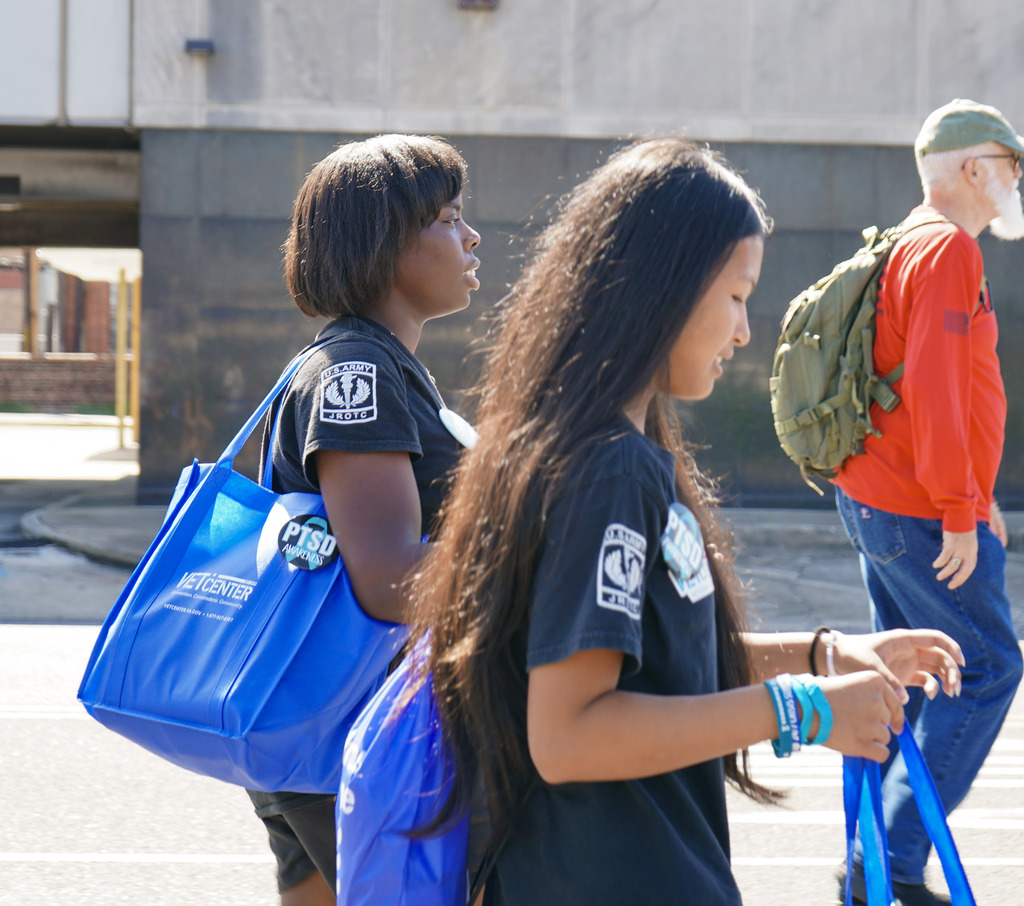 Students walk down a street wearing weighted backpacks during a memorial ruck honoring veterans lost to suicide.