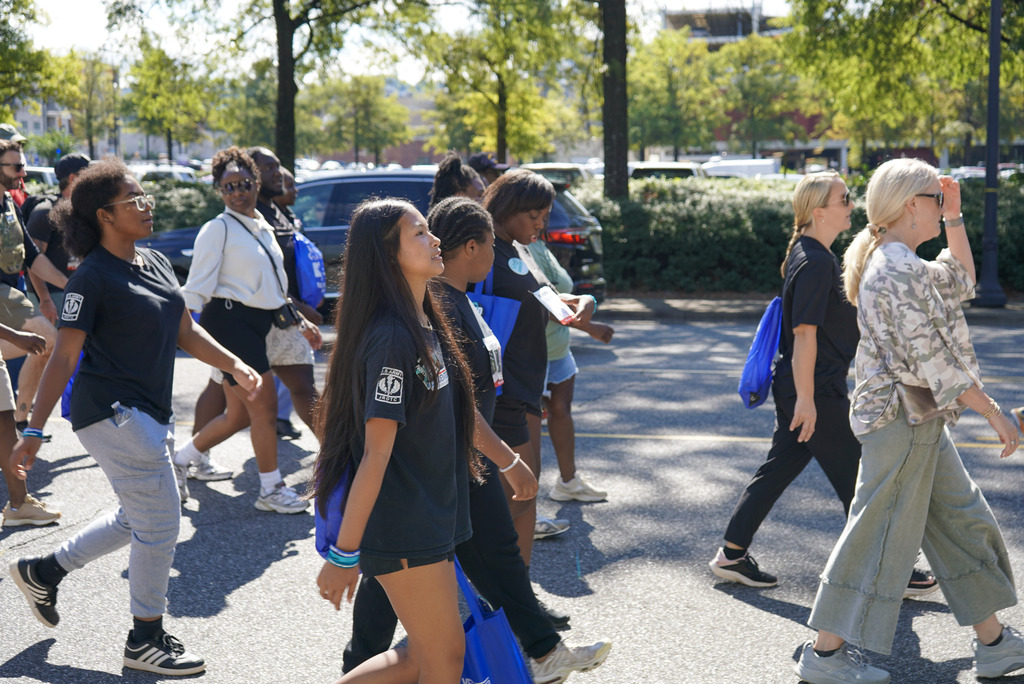 Students and community members walk down a street wearing weighted backpacks to honor veterans lost to suicide.