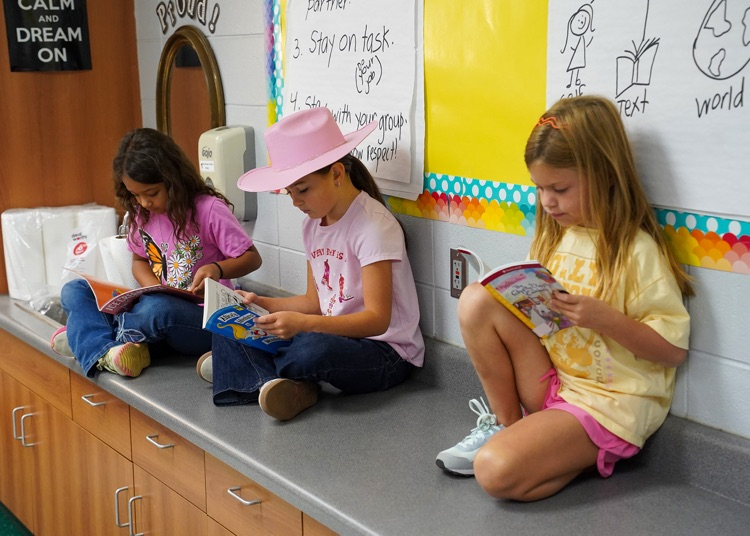 Three students sit on a counter while reading books.