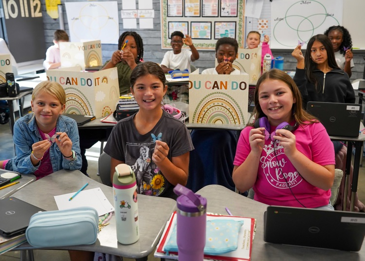 A group of elementary age, students hold up, magnetic butterfly bookmarks they received on Dolly Parton appreciation day at school.