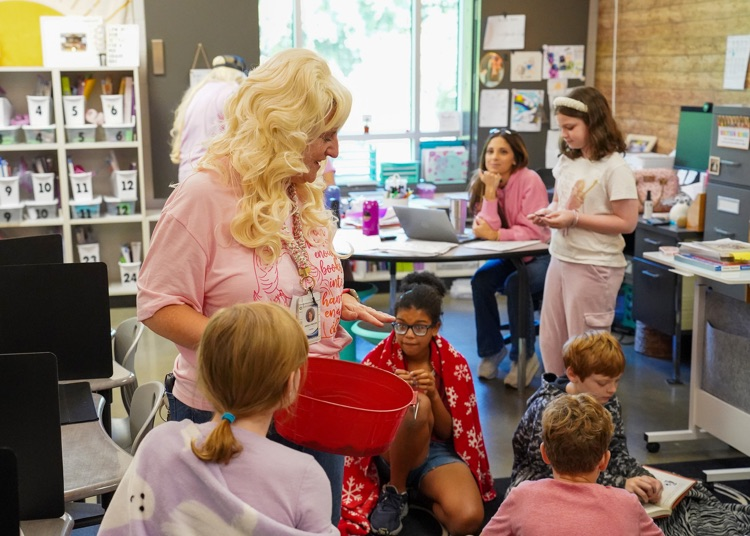 A teacher dressed up as Dolly Parton hands out butterfly bookmarks to students.