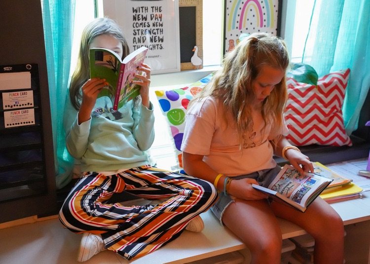 two school students sit in a windowsill and read books.