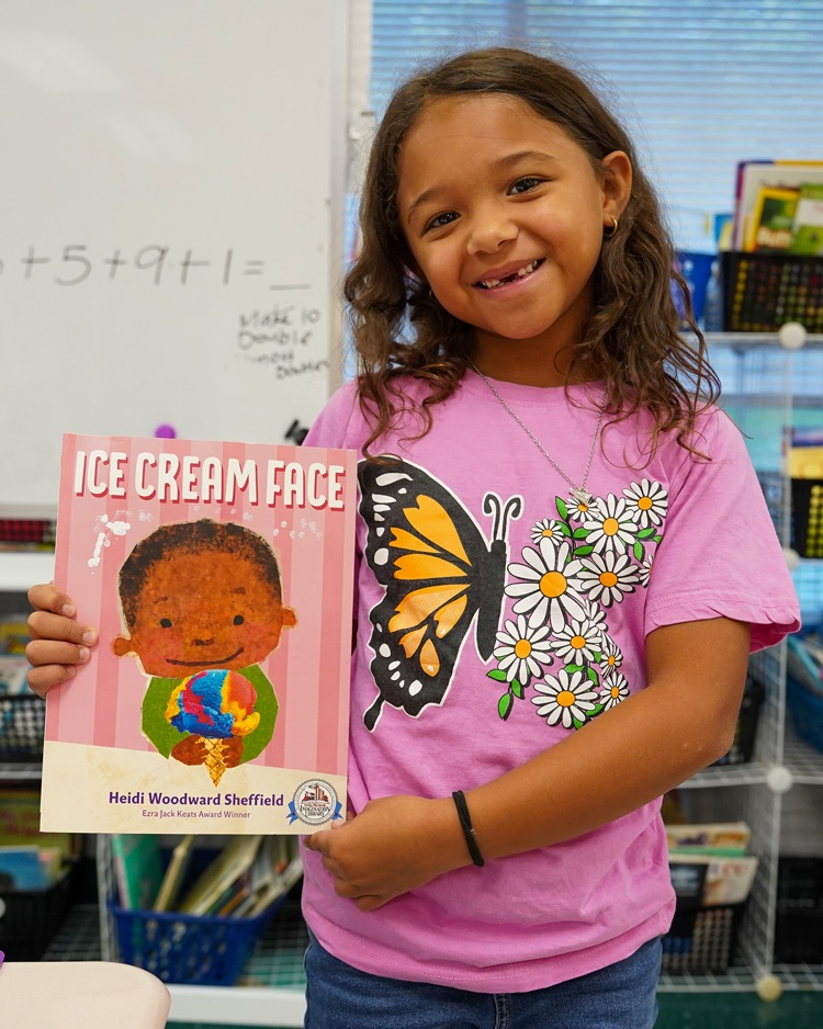 an elementary age school student dressed in a butterfly shirt in honor of Dolly Parton holds up one of her books from Dolly Parton‘s Imagination library.