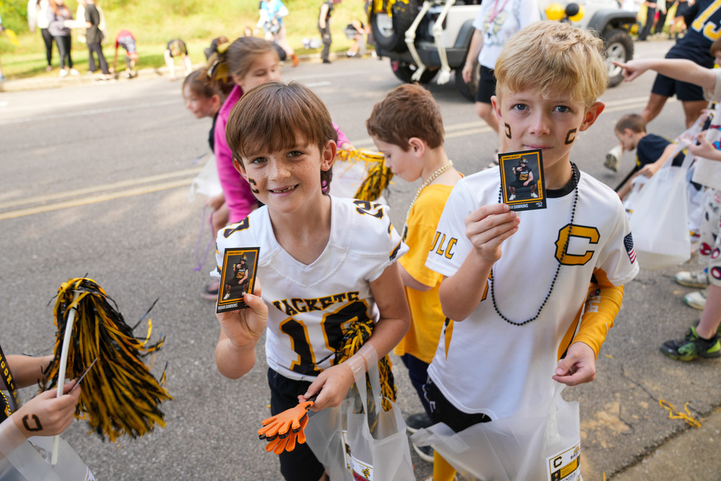 Children smile and hold up playing cards while standing outdoors.