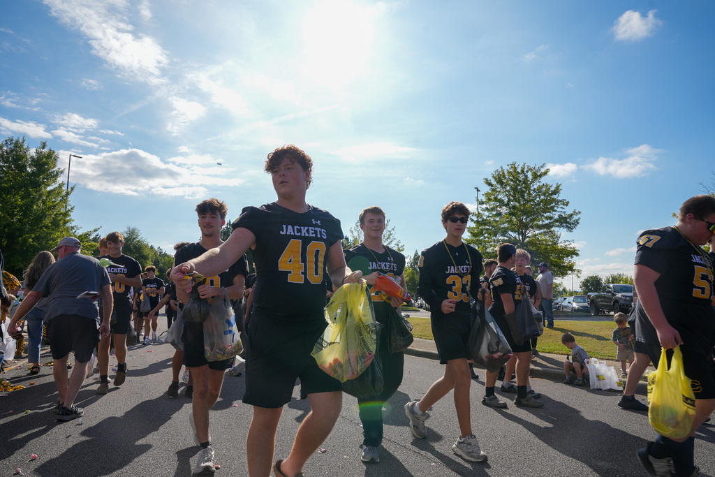 Football players hand out candy during a parade outdoors.