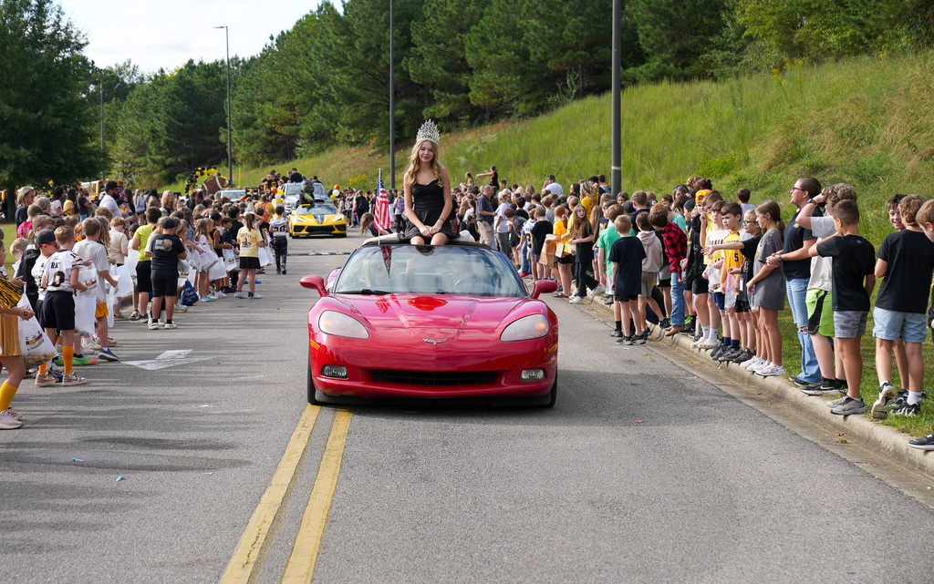A girl wearing a crown rides in a red convertible through a parade route.