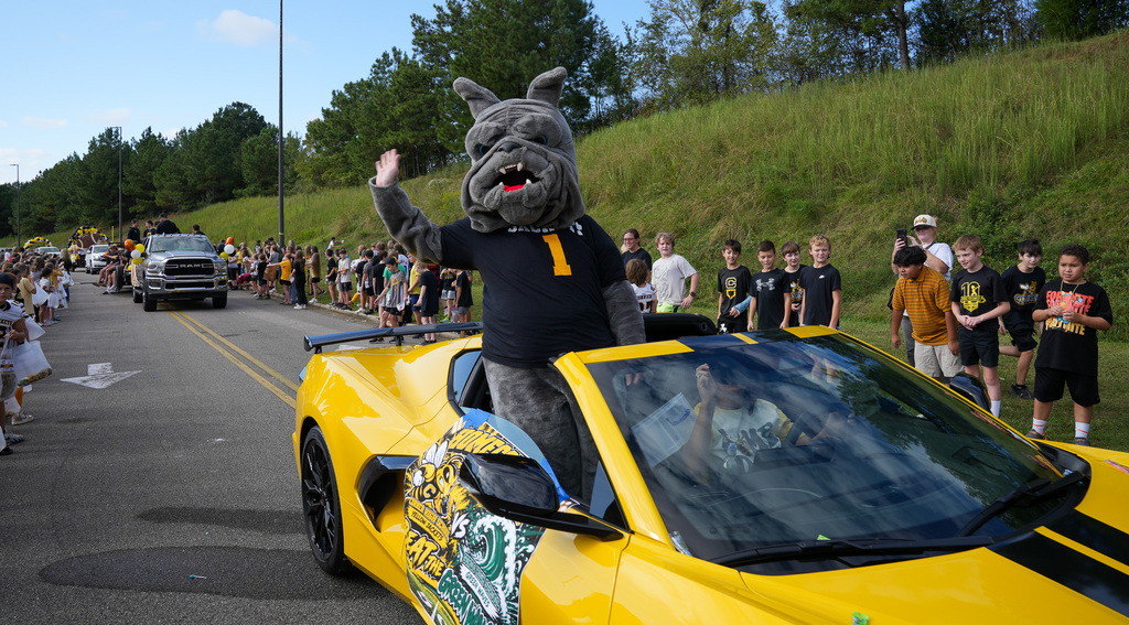 A bulldog mascot waves while riding in a yellow convertible.
