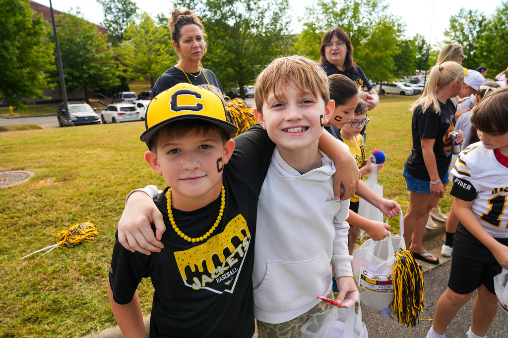 Children hug and smile for a photo while standing outdoors.