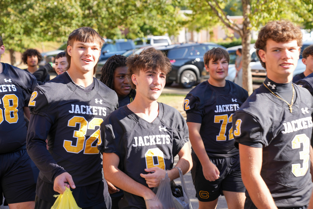 Football players smile while walking down a parade route.