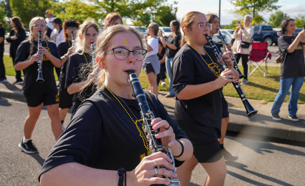 Band members play instruments while walking down a parade route.