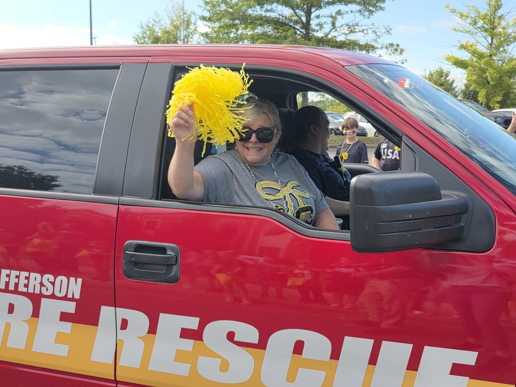 The principal waving a pom pom riding in a truck