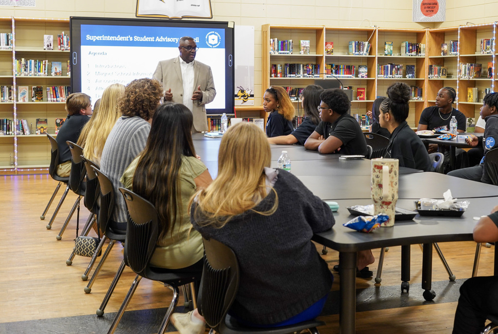 JEFCOED Superintendent Dr. Walter Gonsoulin stands up in a school library and speaks to students as they sit at a table.
