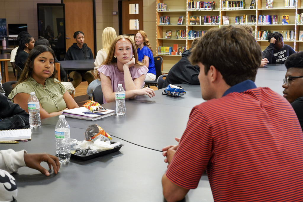 Students sit at a table inside a library.