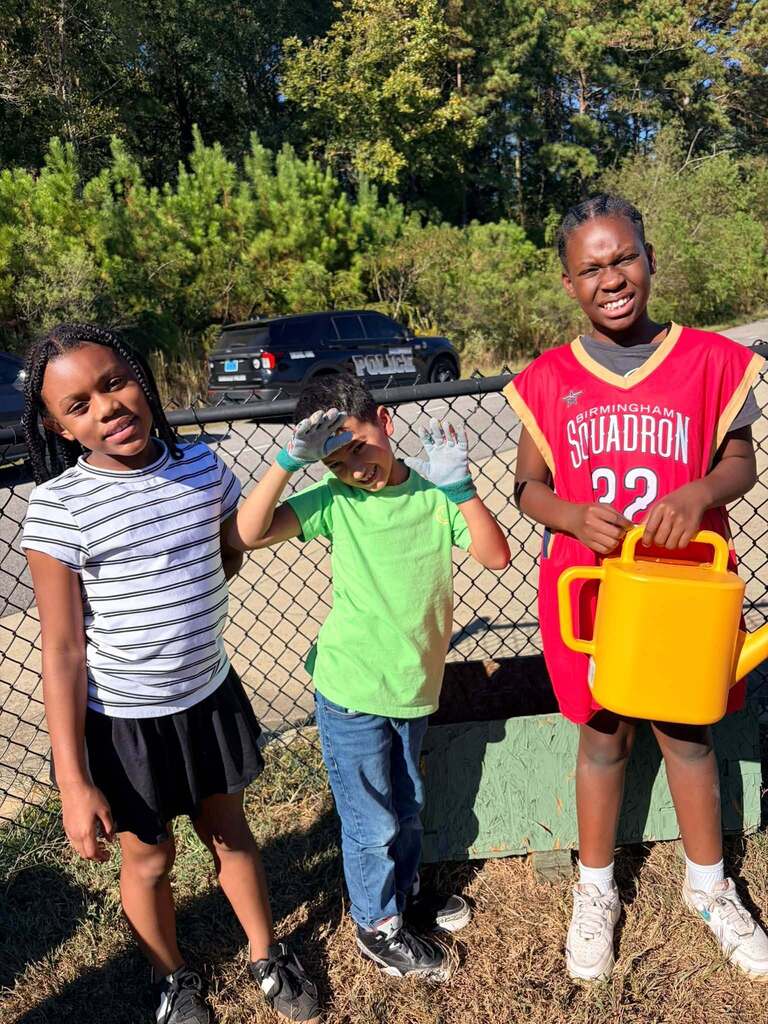 Students smile while working on a garden.