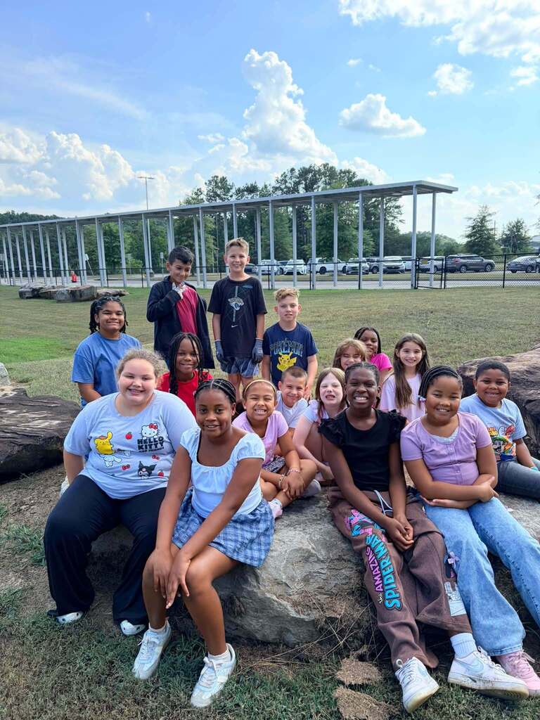 Students sit on rocks outdoors and smile for a photo.
