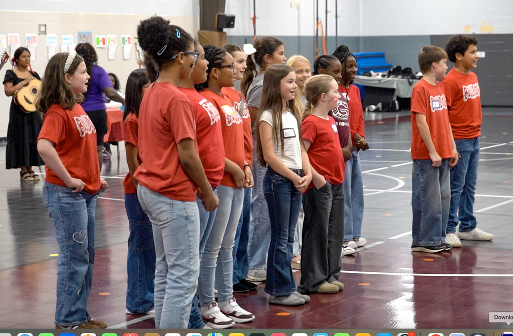 Students perform a song while standing inside a school gym.