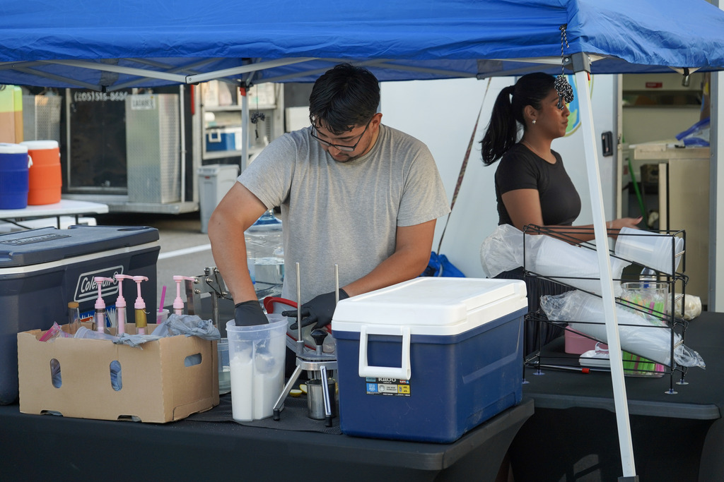 A man and a woman make drinks while standing under a tent.