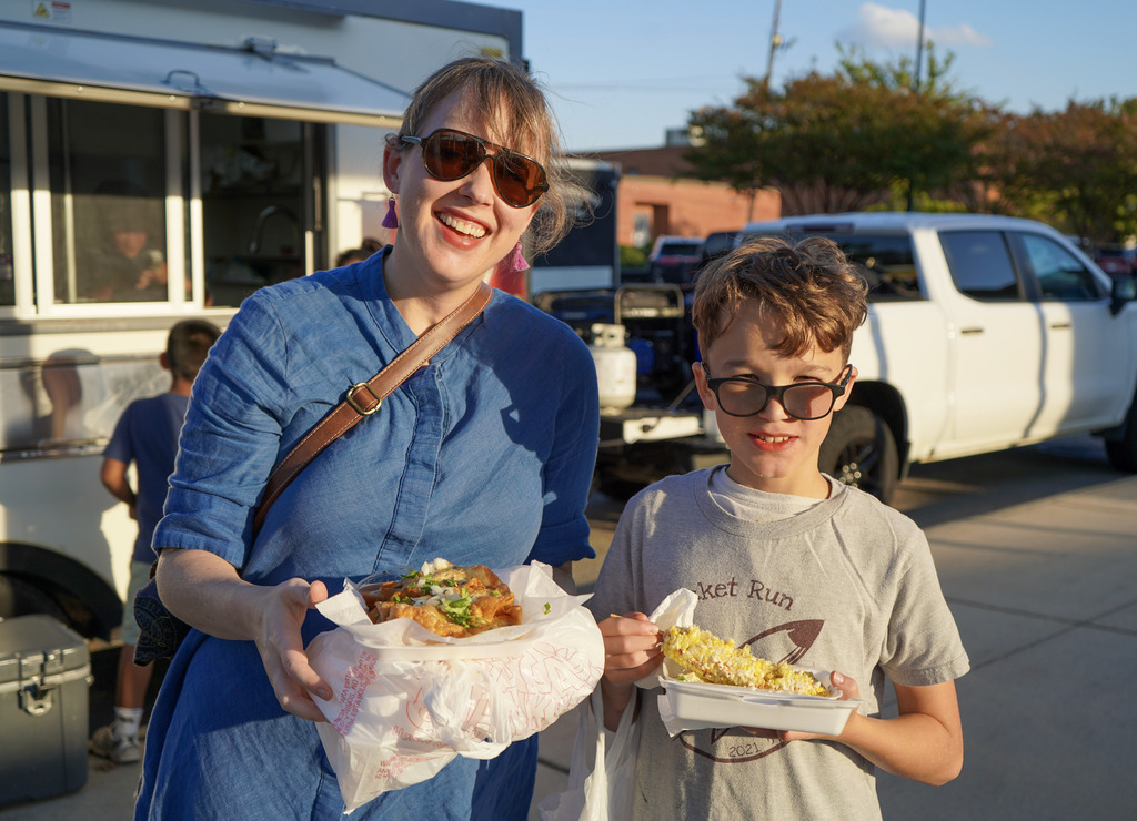 A woman and a child stand together outside a food truck and smile for a photo.