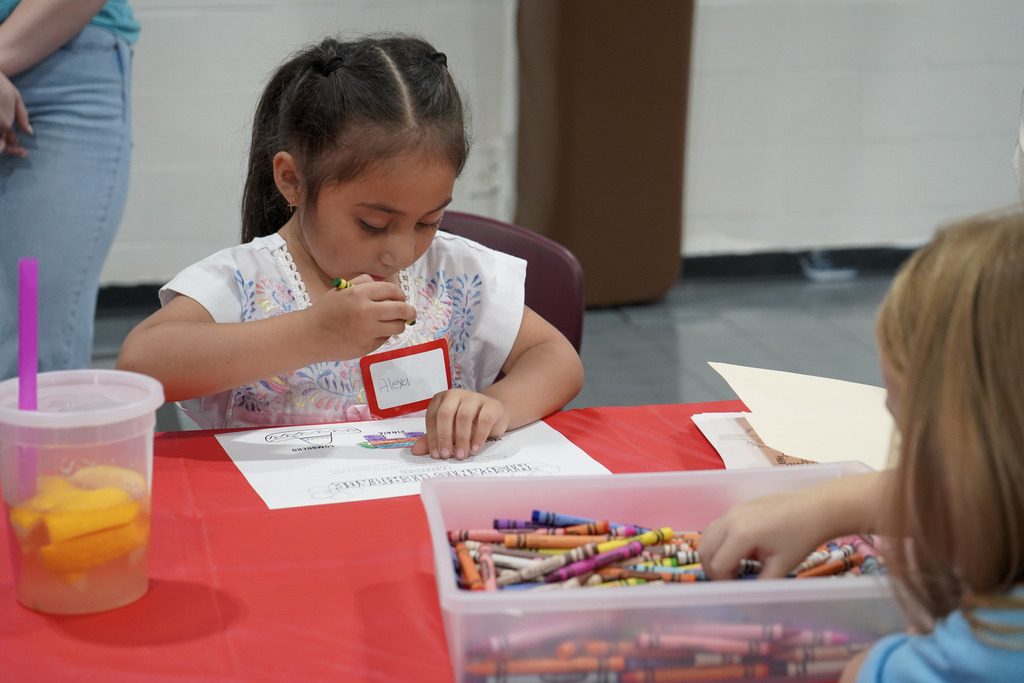 A girl sits at a table and colors a piece of paper.