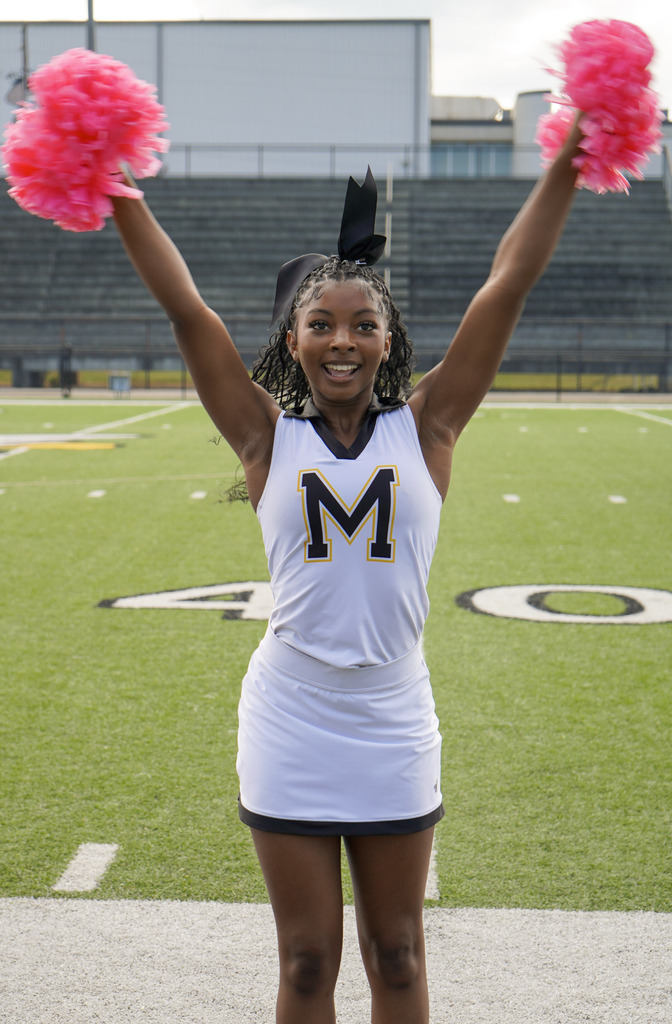 A cheerleader performs a cheer on a football field.