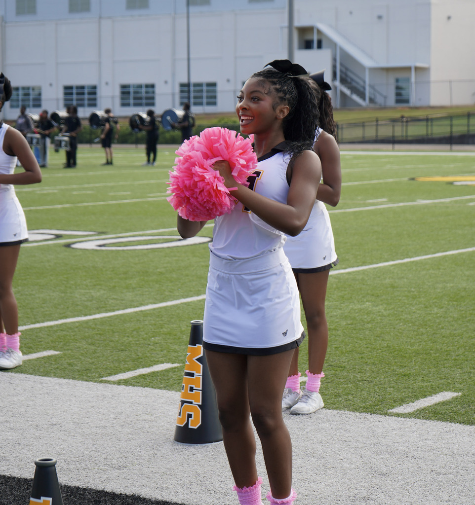 Cheerleaders perform a cheer on a football field.