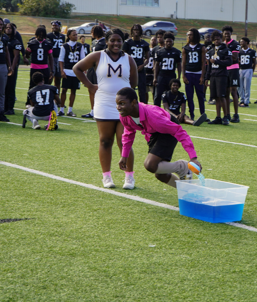 A student sprints down a football field while holding a sponge while playing a pep rally relay game.
