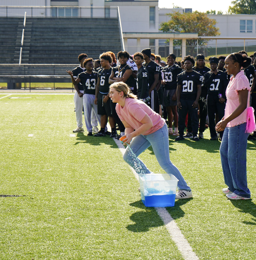 A student sprints down a football field while holding a sponge while playing a pep rally relay game.