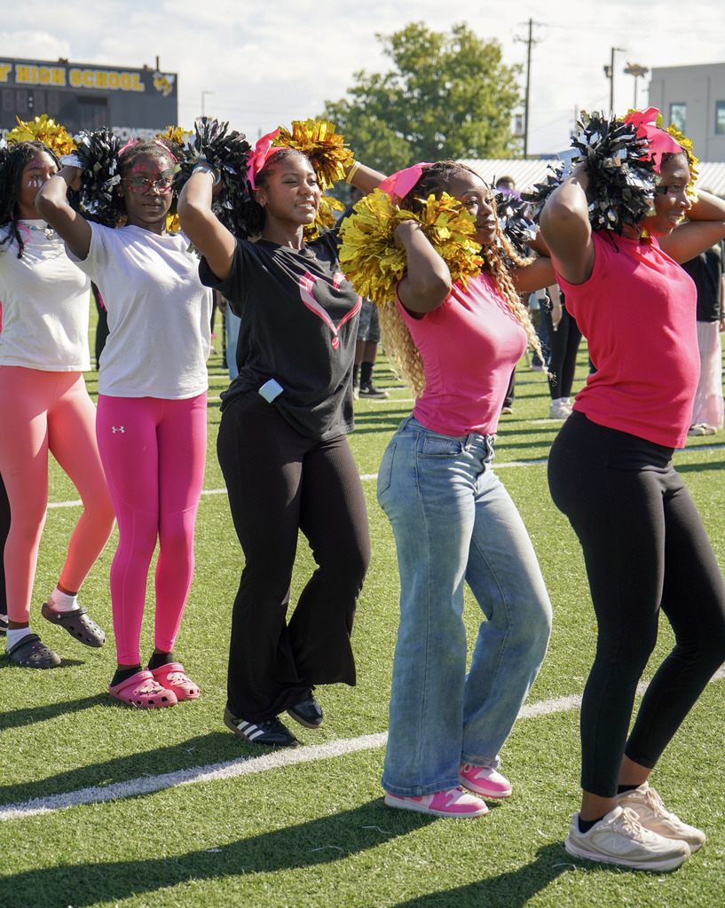 Dance team members smile and perform with pompoms on a football field.
